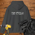 A dark heather coloured hoodie laid flat on a rustic wooden surface, featuring a white tool silhouette across the back. A yellow cordless drill and black work trousers are placed beside it as styling props.
