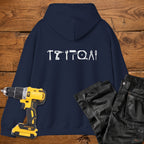 A navy blue coloured hoodie laid flat on a rustic wooden surface, featuring a white tool silhouette across the back. A yellow cordless drill and black work trousers are placed beside it as styling props.