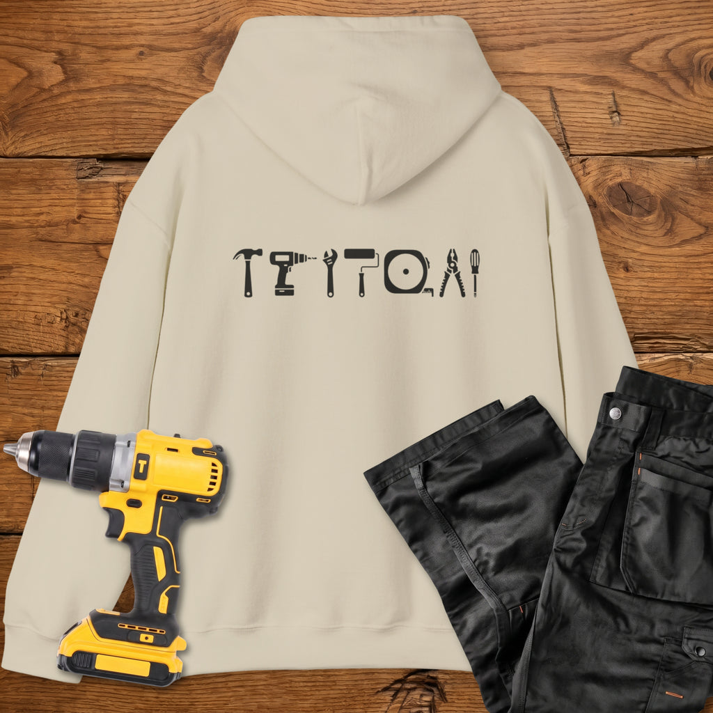 A sand coloured hoodie laid flat on a rustic wooden surface, featuring a white tool silhouette across the back. A yellow cordless drill and black work trousers are placed beside it as styling props.